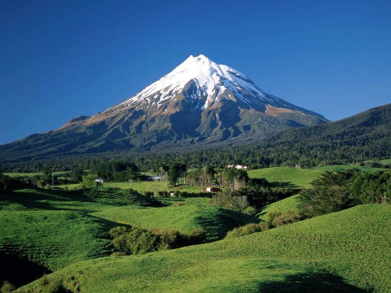 Plaine verdoyante au pied d’une montagne enneigée, symbolisant le passage à travers ce qui bouscule et l’ouverture vers une transformation intérieure plus paisible.
