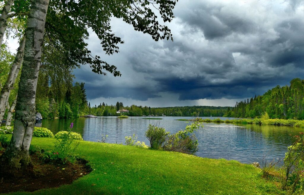 Lac entouré de forêt sous un ciel orageux, reflet des arbres et des nuages dans l’eau
