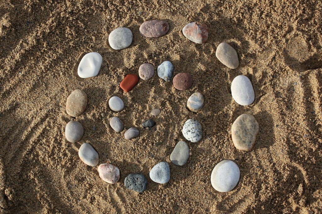 Pierres disposées en spirale sur le sable, symbolisant le mouvement intérieur et l’harmonie retrouvée
