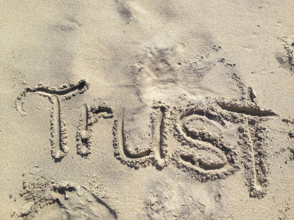 Mot “Trust” (confiance) tracé dans le sable, évoquant la confiance durable et l’ancrage intérieur.