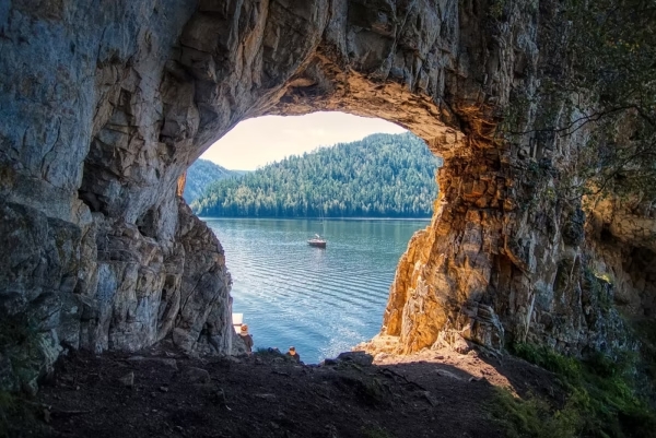 Vue d’un lac à travers une grotte, symbole de la reconnexion intérieure et de la mise en lumière des mémoires.